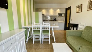 A compact living space with a dining table and chairs, a green sofa, and a kitchenette in the background. - SALLES BEACH 2 (Estartit)
