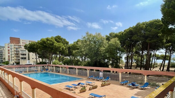 A swimming pool with sun loungers, surrounded by a tiled deck and a railing, with trees and buildings in the background. - SALLES BEACH 3 (Estartit)