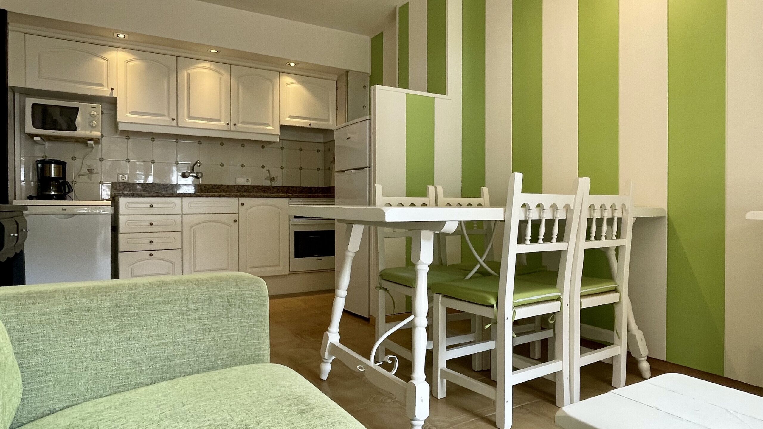 A compact kitchen with white cabinets, a microwave, and a coffee maker. There is a small dining area with a white table and chairs.