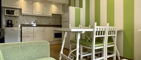 A compact kitchen with white cabinets, a microwave, and a coffee maker. There is a small dining area with a white table and chairs.