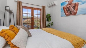 Une chambre à coucher avec un lit, une fenêtre avec des rideaux, un tableau au mur et un appareil de climatisation.