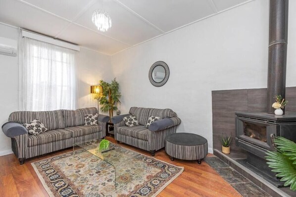 Un salon avec deux canapés à rayures, une table basse, une cheminée et une grande fenêtre avec des rideaux.