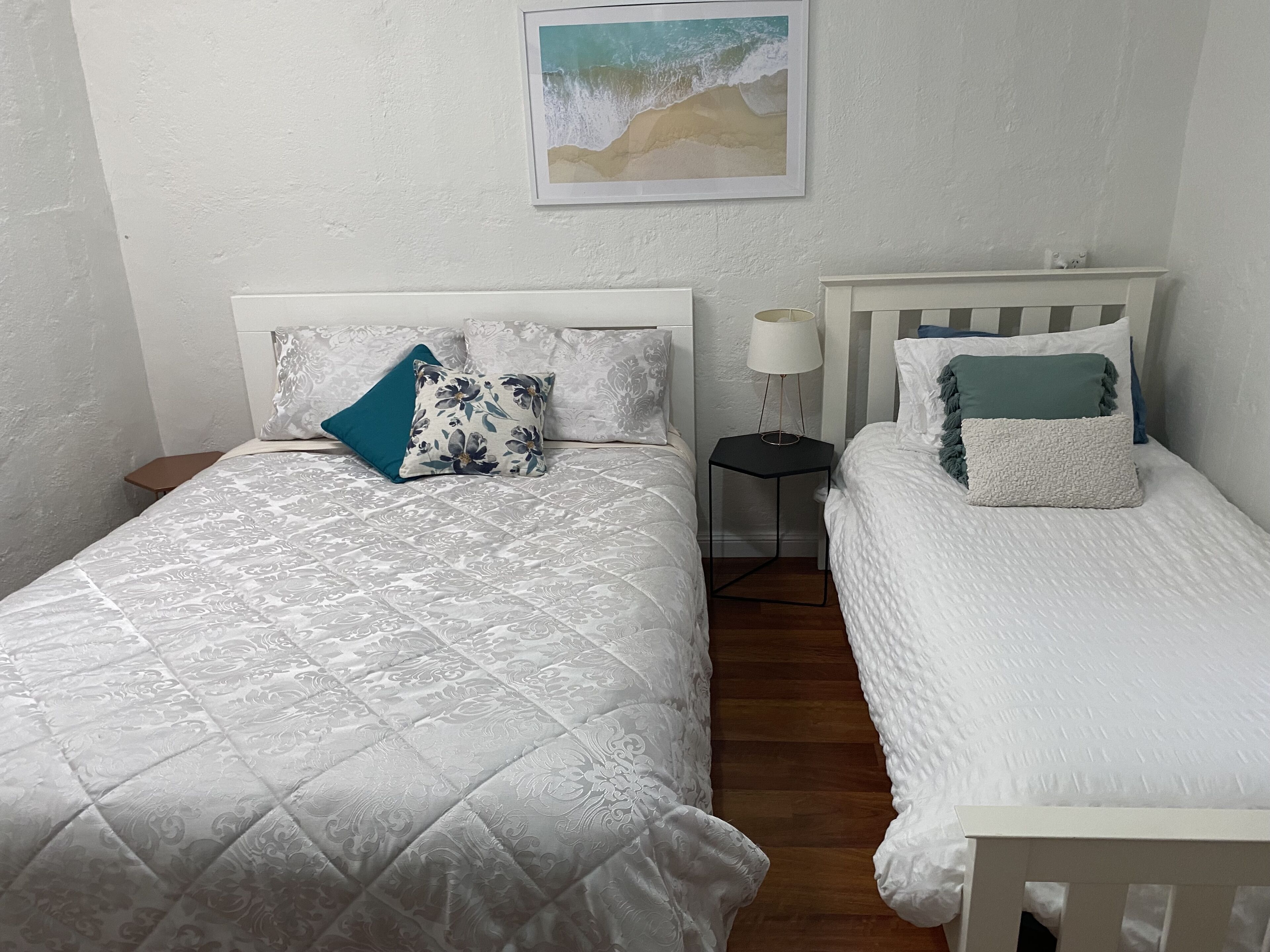 A bedroom with two beds, each with a different style of bedding and pillows. There is a small table with a lamp between the beds.