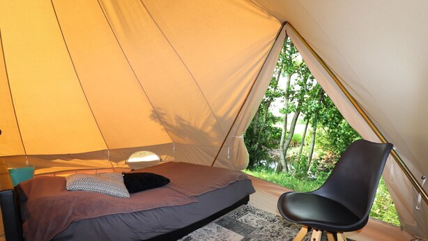 Een tent met een bed, een stoel en een lamp.