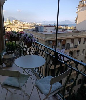 En balkon med et rundt bord og to stole, med udsigt over en by og fjerne bjerge.