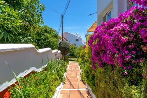 Stroll through lush gardens to a charming Mediterranean-style building with a tiled roof.