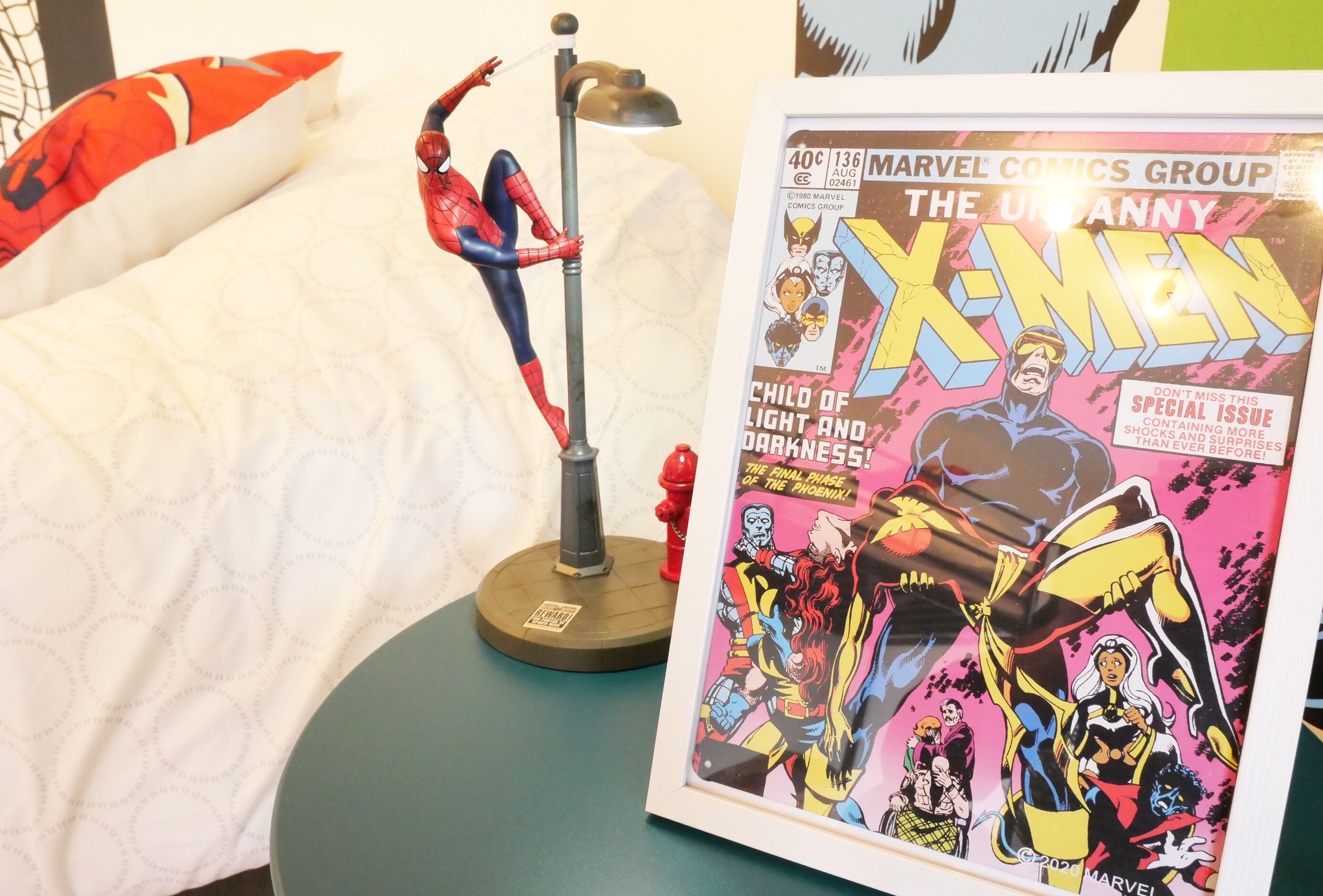A bed with a Spider-Man figurine, a framed X-Men comic book, and a lamp.