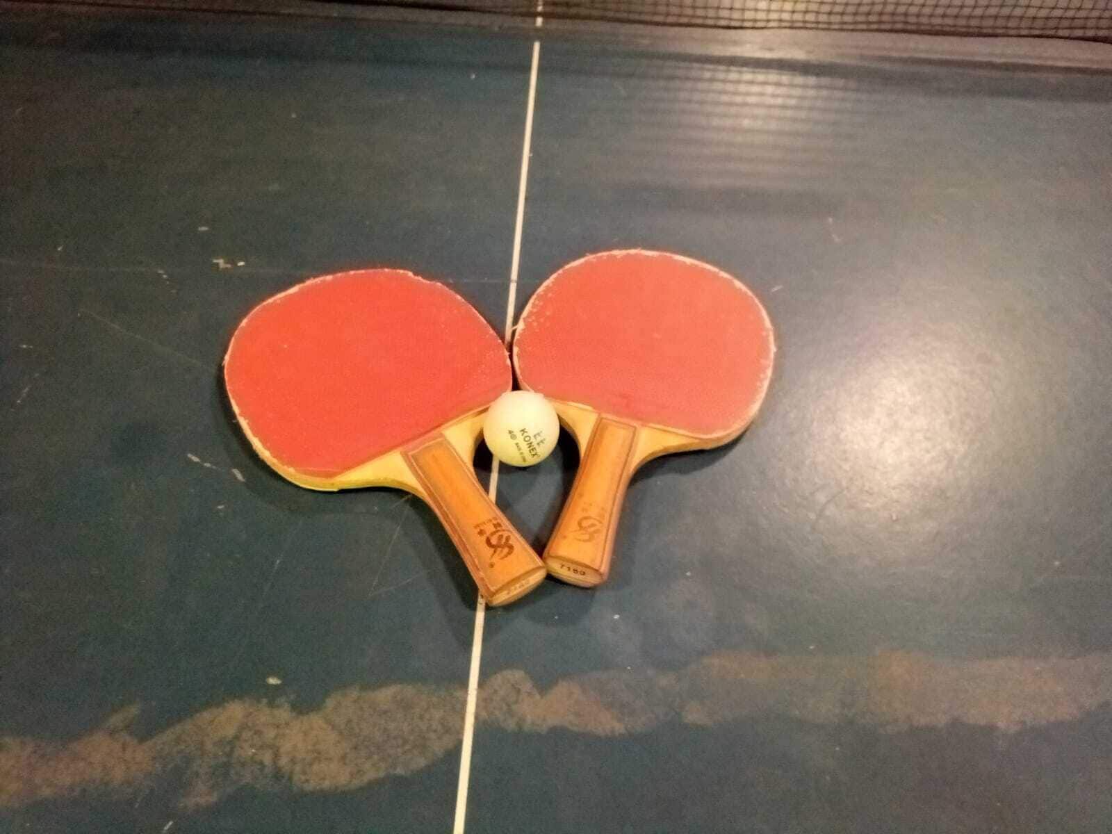 Una mesa de tenis de mesa con dos paletas rojas y una pelota.