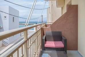 En balkon med en fletstol, et glasbord og havudsigt.