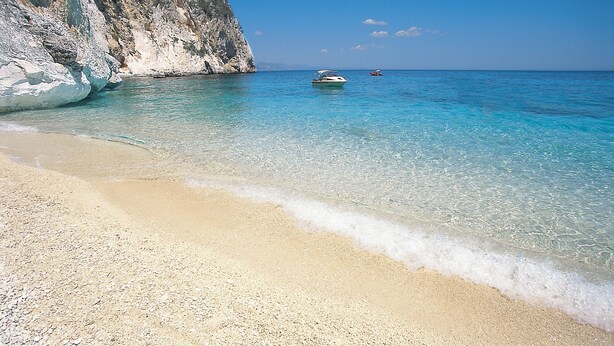 Ein Strand mit klarem, türkisblauem Wasser, einem Boot und einer felsigen Klippe.
