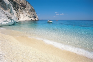 Ein Strand mit klarem, türkisblauem Wasser, einem Boot und einer felsigen Klippe.