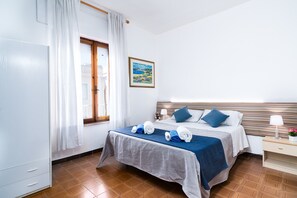 A hotel room with a bed, a nightstand, a lamp, a painting on the wall, and a window with curtains.
