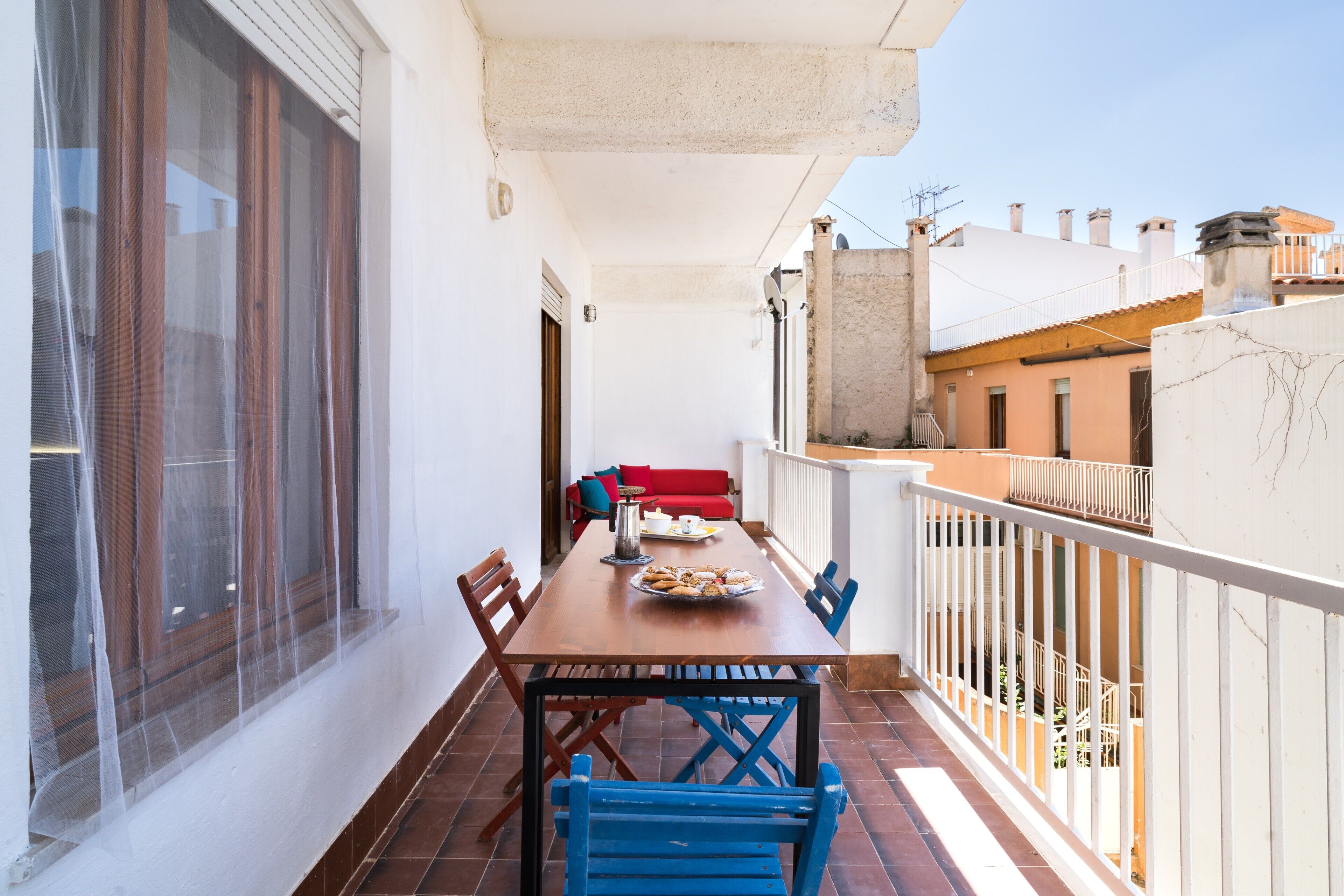 A balcony with a dining table, chairs, and a red sofa.