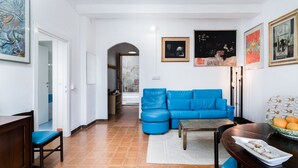 Ein Wohnzimmer mit einem blauen Sofa, einem Esstisch mit Obstschale und Kunstwerken an den Wänden.