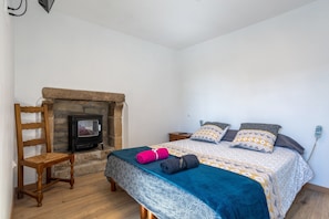 Un dormitorio con una cama, una silla, una chimenea pequeña y una mesita de noche.
