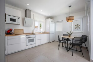A modern kitchen with white cabinetry, a wooden countertop, a built-in oven, a microwave, and a dining area with a table and chairs.