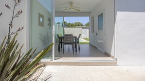 A modern house with a glass door leading to a patio area with a table and chairs. - Casita Meraki 3 with Heated Indoor Pool, Garden, Terrace, and Wi-Fi (Chiclana de la Frontera)
