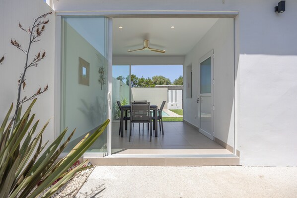 A modern house with a glass door leading to a patio area with a table and chairs.