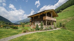 A wooden cabin with a balcony, surrounded by a well-maintained lawn and a stone foundation. - Chalet 'Zu Wosser' with Mountain Views, Private Terrace and Garden (San Leonardo in Passiria)