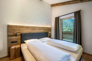 A double bed with a wooden headboard, a nightstand, and a window with a view of a forest. - Chalet 'Zu Wosser' with Mountain Views, Private Terrace and Garden (San Leonardo in Passiria)