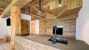 A modern kitchen with wooden accents, a built-in stove, and pendant lighting. - Chalet 'Zu Wosser' with Mountain Views, Private Terrace and Garden (San Leonardo in Passiria)