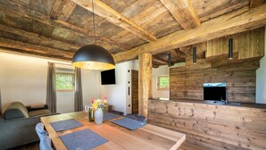 A wooden dining table with a vase of flowers, a sofa, and a television in a rustic interior. - Chalet 'Zu Wosser' with Mountain Views, Private Terrace and Garden (San Leonardo in Passiria)