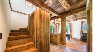 A wooden staircase leading to a room with a view of greenery, a dining area, and a large wooden beam ceiling. - Chalet 'Zu Wosser' with Mountain Views, Private Terrace and Garden (San Leonardo in Passiria)
