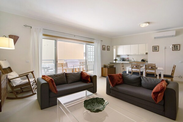 A modern living room with two sofas, a glass coffee table, and a dining area in the background.