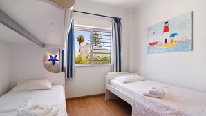 Un dormitorio con dos camas, una ventana con cortinas, un cuadro de un faro y un adorno con forma de estrella.