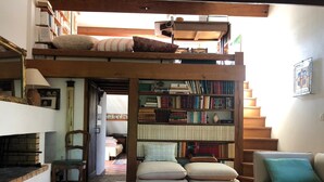 Un dormitorio tipo loft con cama en alto, una estantería, una mesa de centro de vidrio, un sofá y una chimenea.