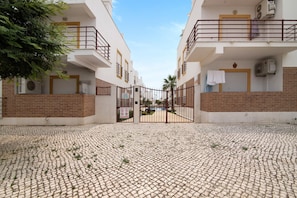 A gated courtyard with cobblestone flooring, a central gate, and two-story buildings with balconies and air conditioning units.