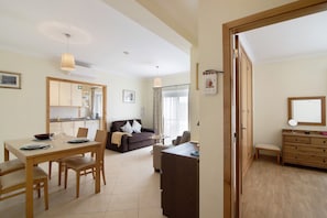 A living room with a sofa, a dining table, and a kitchen in the background.