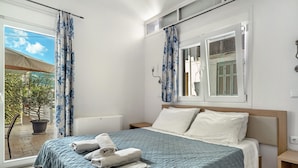 Una camera da letto con un letto, cuscini, un comodino, una finestra con tende e vista sull'esterno.