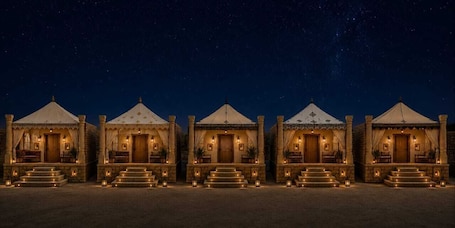 A row of five illuminated tents with steps leading to the entrance, set against a night sky.
