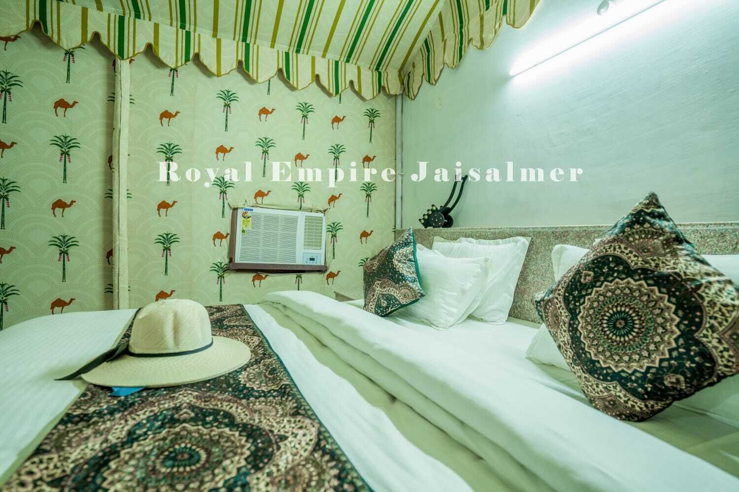 Una habitación de hotel con papel tapiz estampado, una cama con ropa blanca, almohadas decorativas, un sombrero sobre la cama y un equipo de aire acondicionado en la pared.