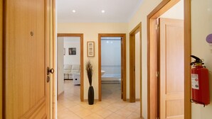 Un couloir avec des portes en bois, un extincteur et un vase décoré de branches.