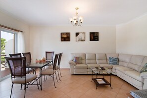 Una sala de estar con una mesa de vidrio para comer, cuatro sillas, un sofá, una mesa de centro y una araña.