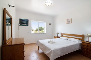 Um quarto com uma cama, cômoda, mesa de cabeceira, janela com vista e luminária de teto.