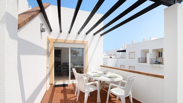 Une terrasse avec une table et des chaises, une porte donnant sur un espace intérieur et un ciel dégagé.