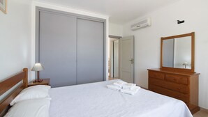 Un lit bien fait, avec du linge de lit blanc, une commode en bois avec un miroir et une porte fermée.
