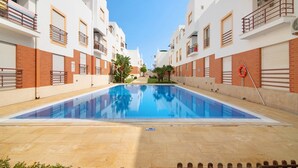 Une piscine entourée de bâtiments blancs dotés de balcons, un ciel dégagé et une bouée de sauvetage placée au bord de la piscine.