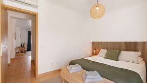 Une chambre à coucher avec un lit, une table de chevet, un luminaire suspendu et une vue sur une autre pièce.