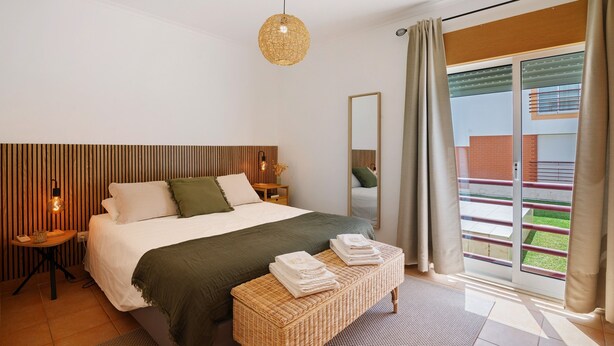 Une chambre à coucher comprenant un lit, des tables de chevet, un luminaire suspendu, un banc et une porte-fenêtre coulissante donnant sur l’extérieur.