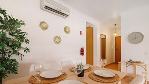 Un coin repas avec une table en bois dressée pour quatre personnes, entourée de chaises blanches, agrémenté d’œuvres d’art décoratives sur les murs et d’un extincteur.