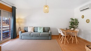 Un salon comprenant un canapé, une table à manger, des chaises, un luminaire suspendu et une plante.
