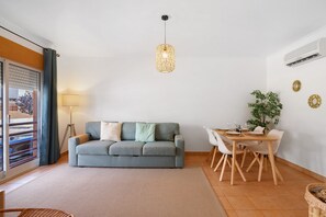 A living room with a sofa, dining table, chairs, a hanging light fixture, and a plant.