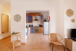 A kitchen with a microwave, stove, and cabinets. There is a wicker chair and a small table with a basket.