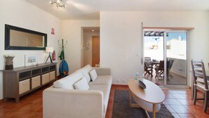 Una sala de estar con sofá, una mesa de comedor, un televisor y un balcón con vistas.
