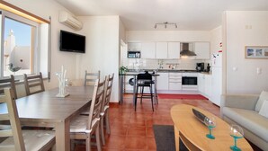 Una cocina moderna con armarios blancos, un comedor con muebles de madera y una sala de estar con sofá y mesa de centro.
