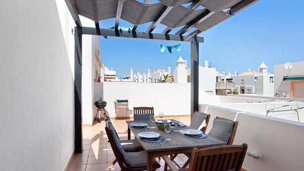 Una terraza con mesa dispuesta para comer, sillas y una estructura de pérgola.